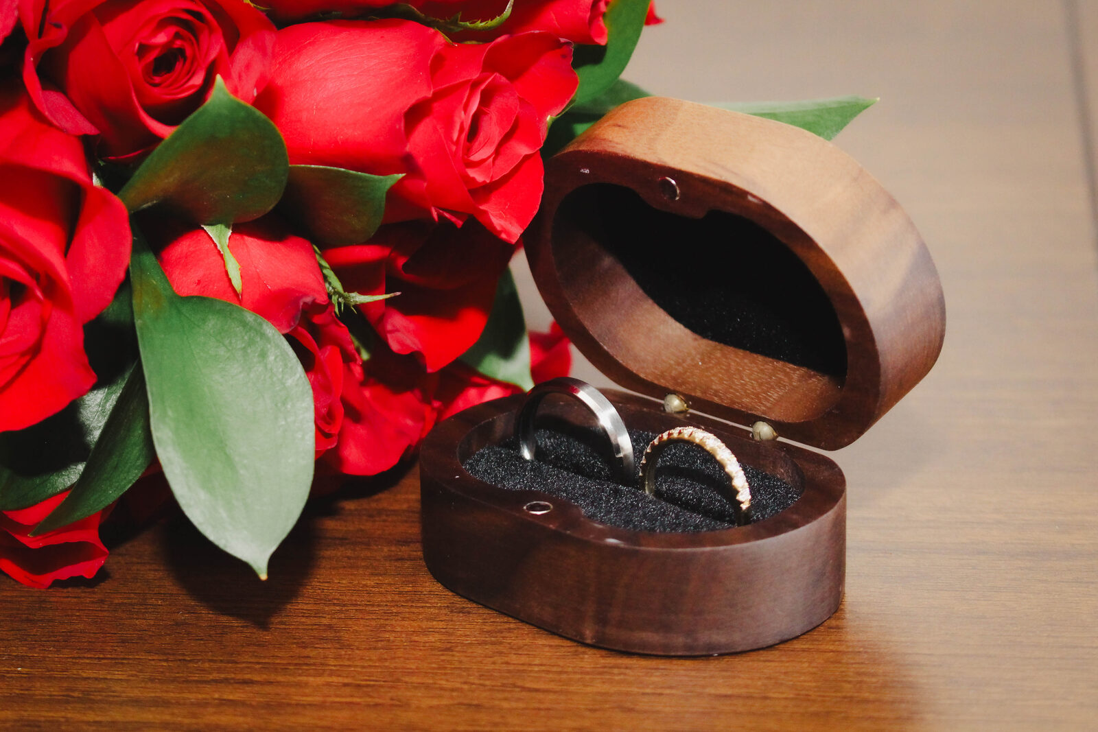 Wedding rings in a wooden box beside red roses